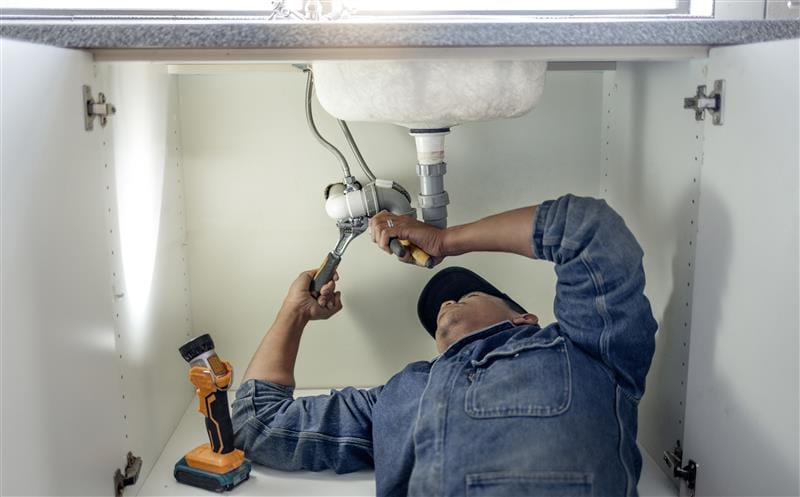 Plumber repairing pipes beneath a bathroom sink in Marietta