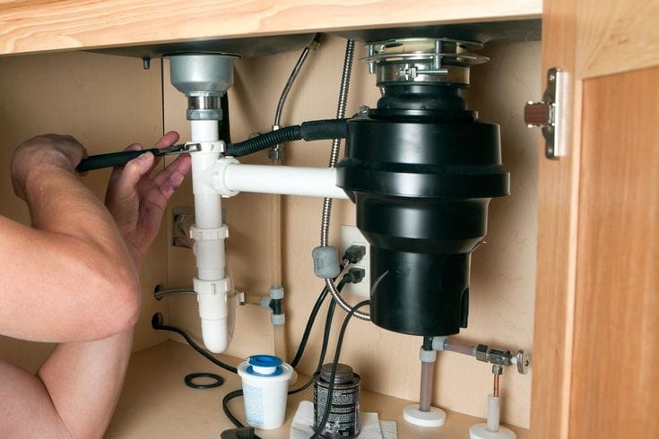 Plumber installing a garbage disposal beneath a kitchen sink in Marietta