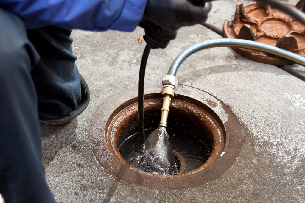 Plumber hydro jetting a sewer line through a manhole in Marietta