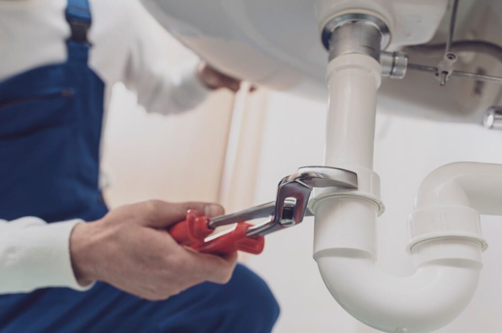 Plumber repairing a white drain pipe beneath a sink in Marietta